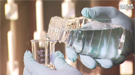 Gloved hands of a scientist pouring a glass of clear liquid into a beaker.