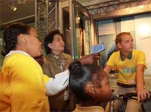 Young female student riding display bike with classmates looking on.